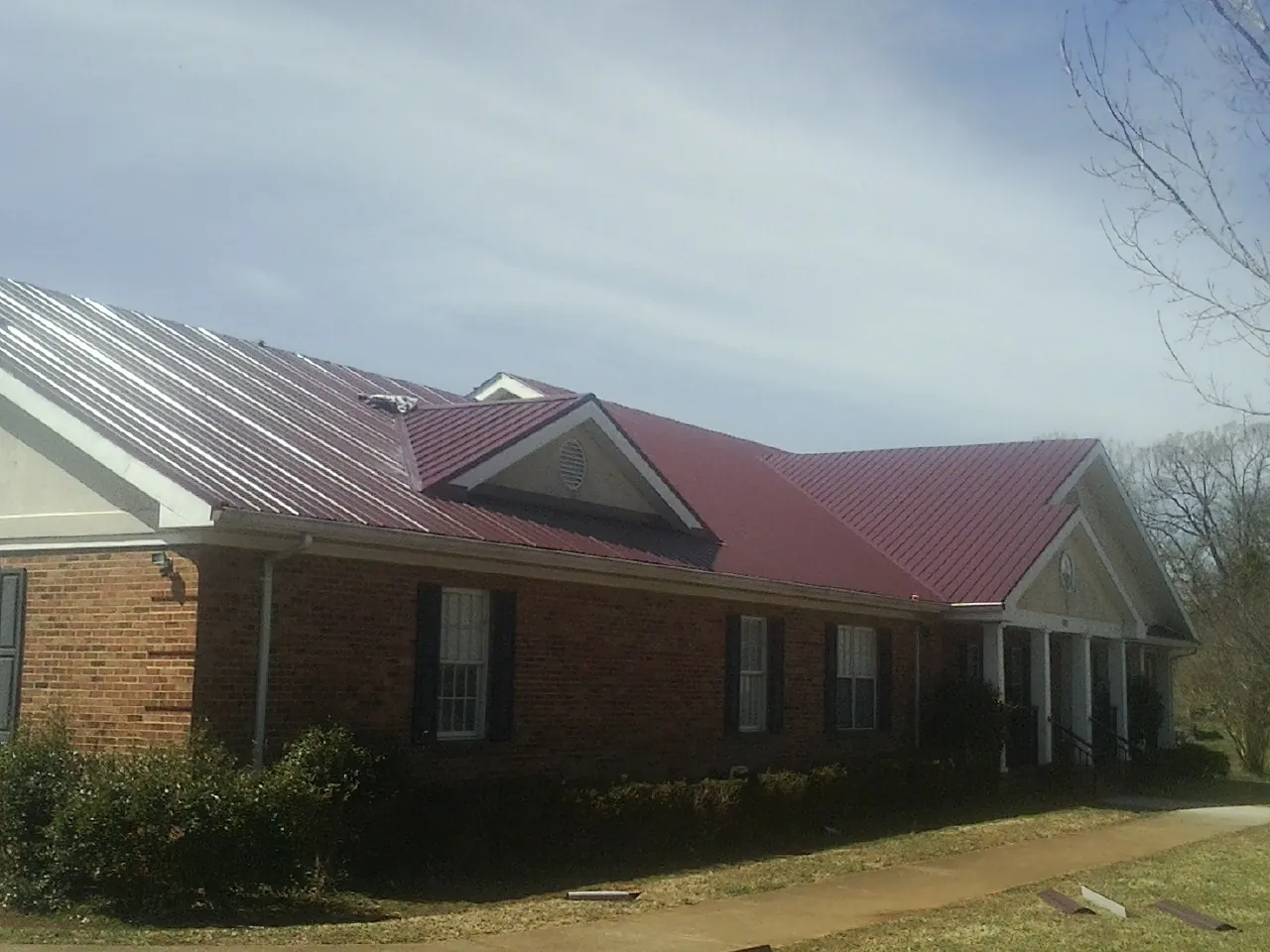Red metal roof with gabled entries on a long brick building, from a Hail Damage Roof Repair job in Ashland